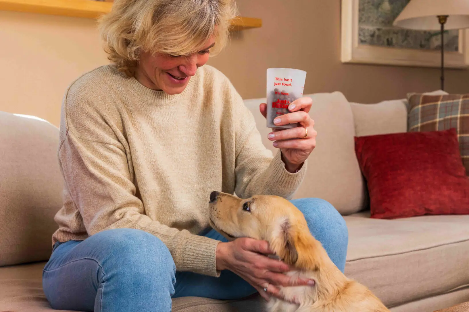 Eine Hundebesitzerin streichelt ihren Welpen und hält dabei einen Messbecher voll mit Trockenfutter in der Hand.