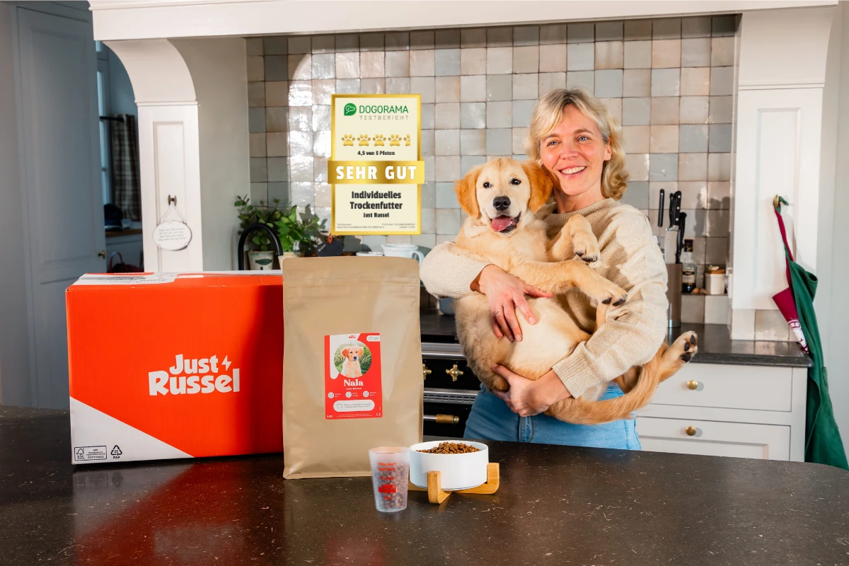 Eine Frau hält ihren Golden Retriever Welpen auf dem Arm. Vor ihnen auf dem Tisch steht das personalisierte Futter von Just Russel.